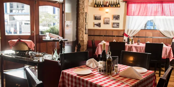 Salón de Sapore Trattoria San José, con manteles a cuadros y la estación de la rueda de queso